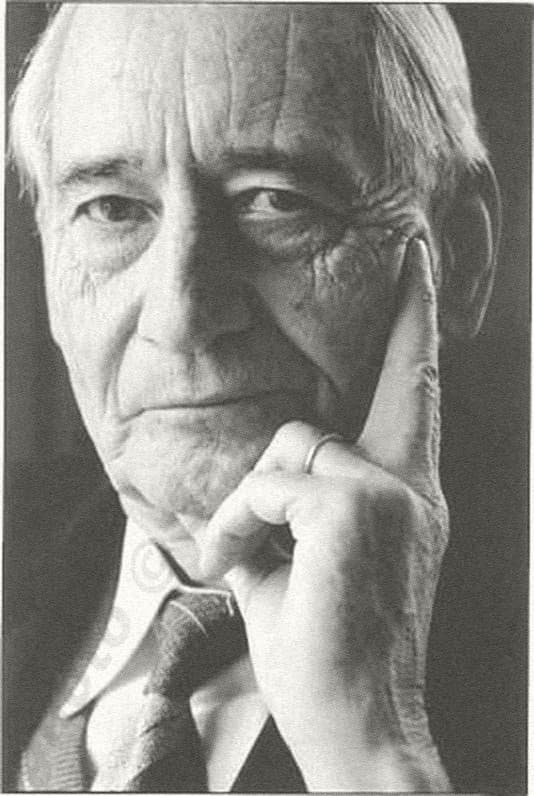 Portrait en noir et blanc de Jean Pictet, âgé, la main contre la joue, le regard vers l’objectif.